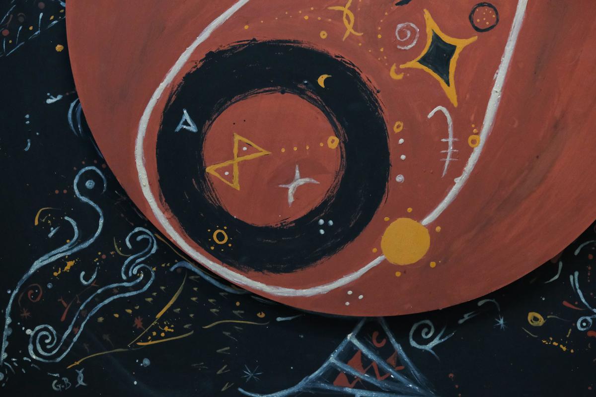A close view of the painting: a black ring on the terracotta circle, containing a yellow triangle motif and a white four-pointed star, with the artist's initials painted below.