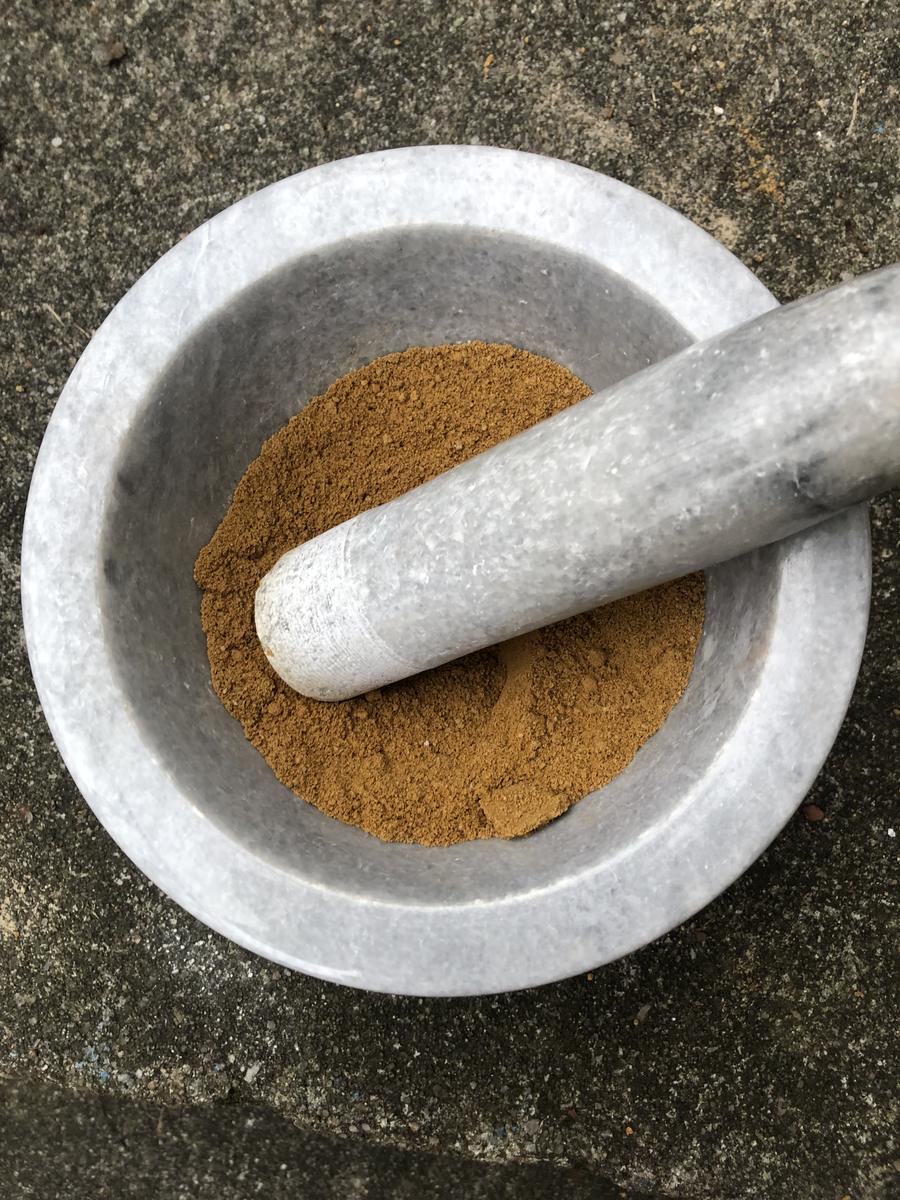 A white marble mortar and pestle on stone, filled with bright yellow ochre powder.