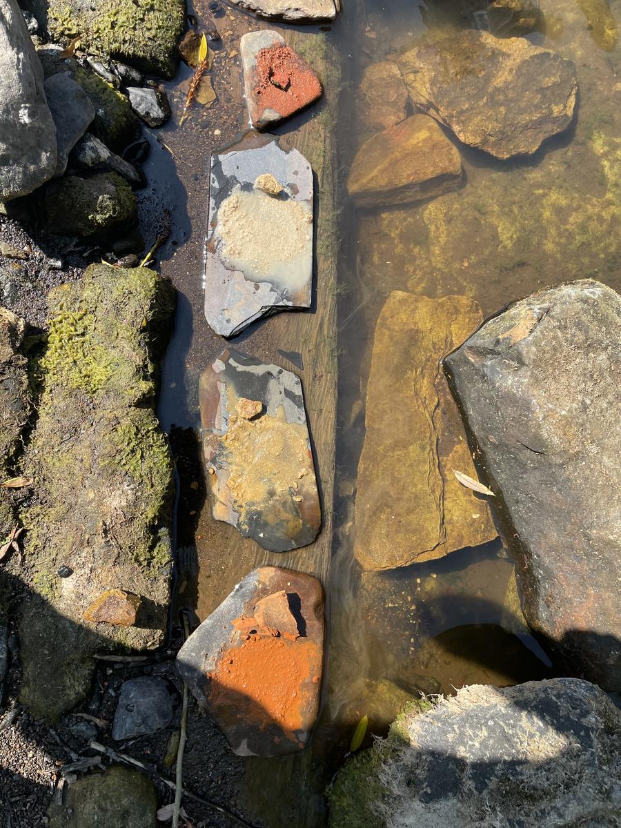 Wet stones in a shallow stream, streaked with orange, yellow and white mineral colour.