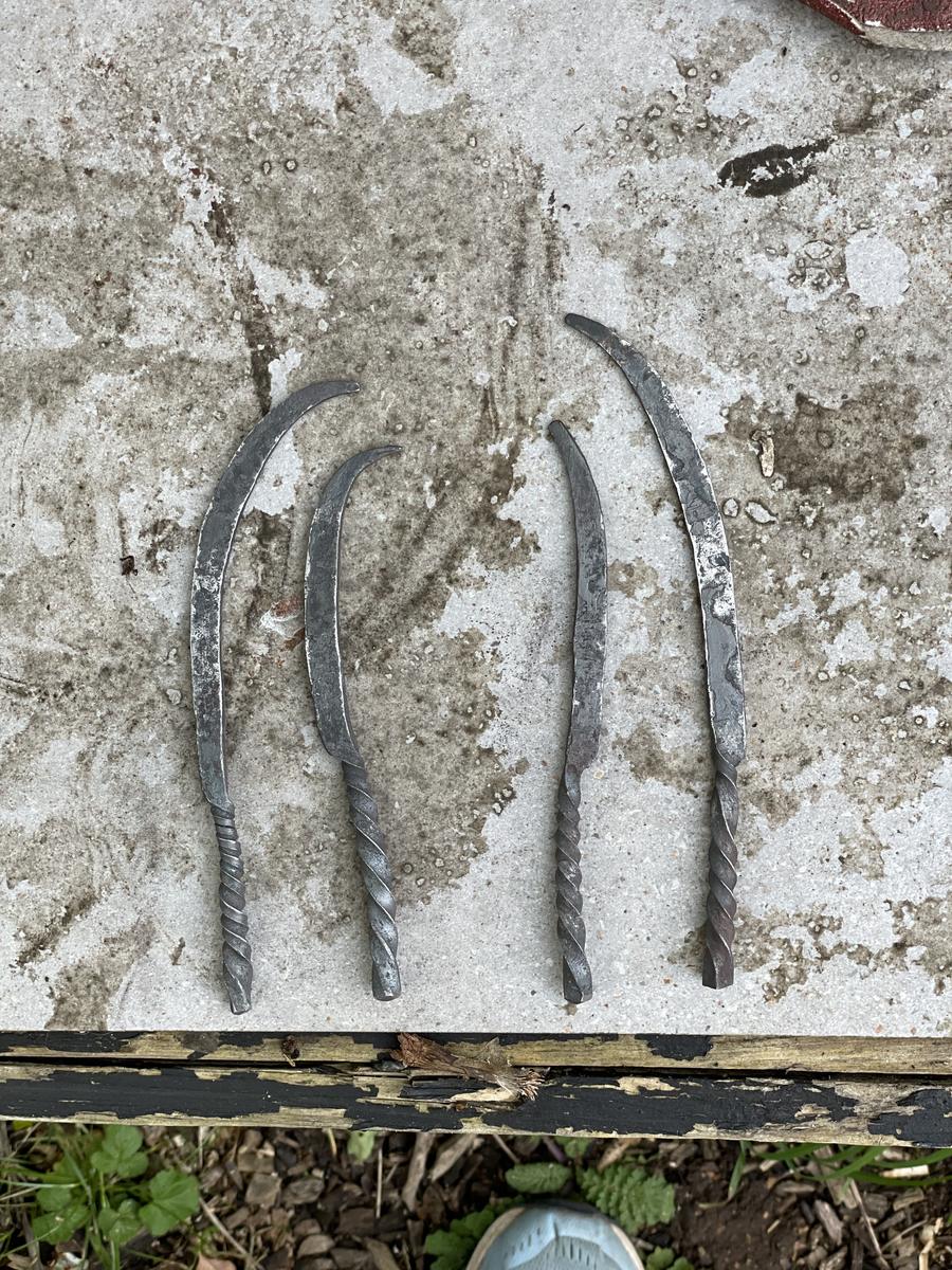 Four finished curved metal blades of different lengths laid out side by side on a concrete surface.