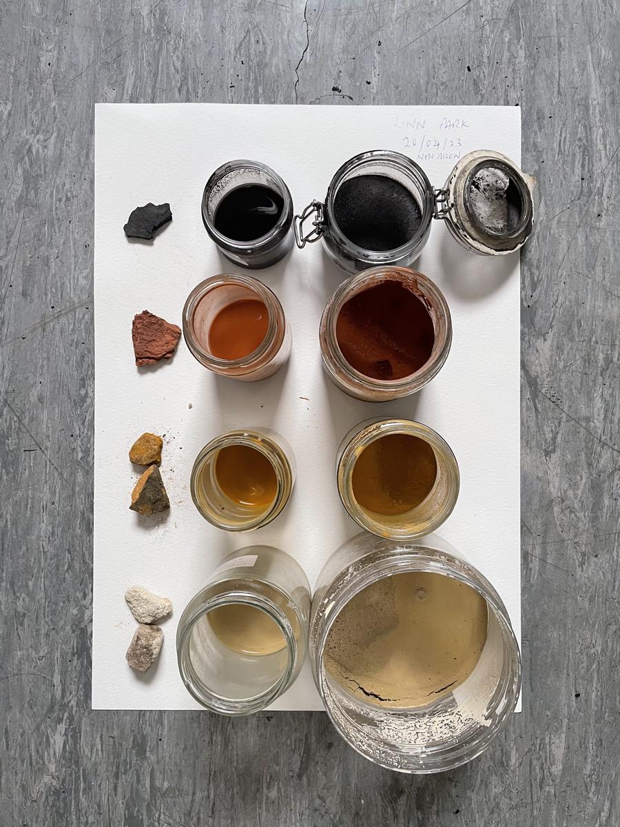 Jars of pale grey, yellow, orange and black pigment laid out on white board with the stones they were ground from.