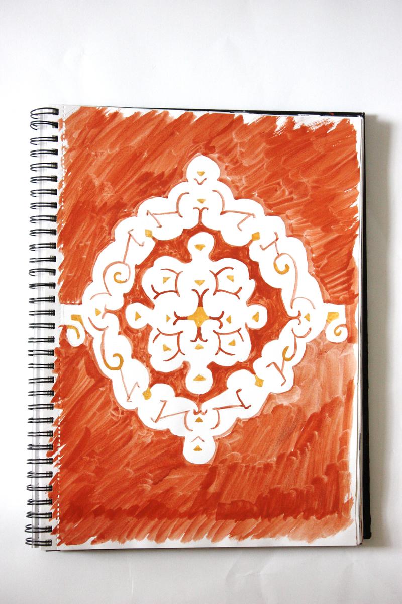 A sketchbook page washed in red ochre, with a large symmetrical white ornamental motif painted at its centre, picked out with yellow triangles and fine red lines.