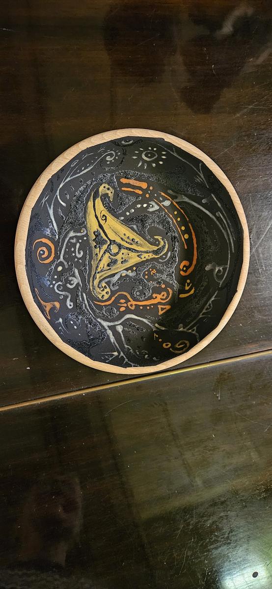 A round wooden bowl painted in blue-black, with a curved yellow ochre form at its centre surrounded by white and orange marks.