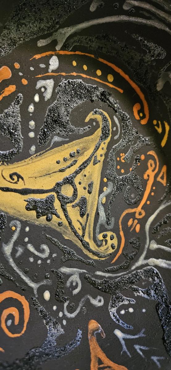 Close detail of a painted bowl — a yellow ochre curve outlined in white, on a dark speckled ground.